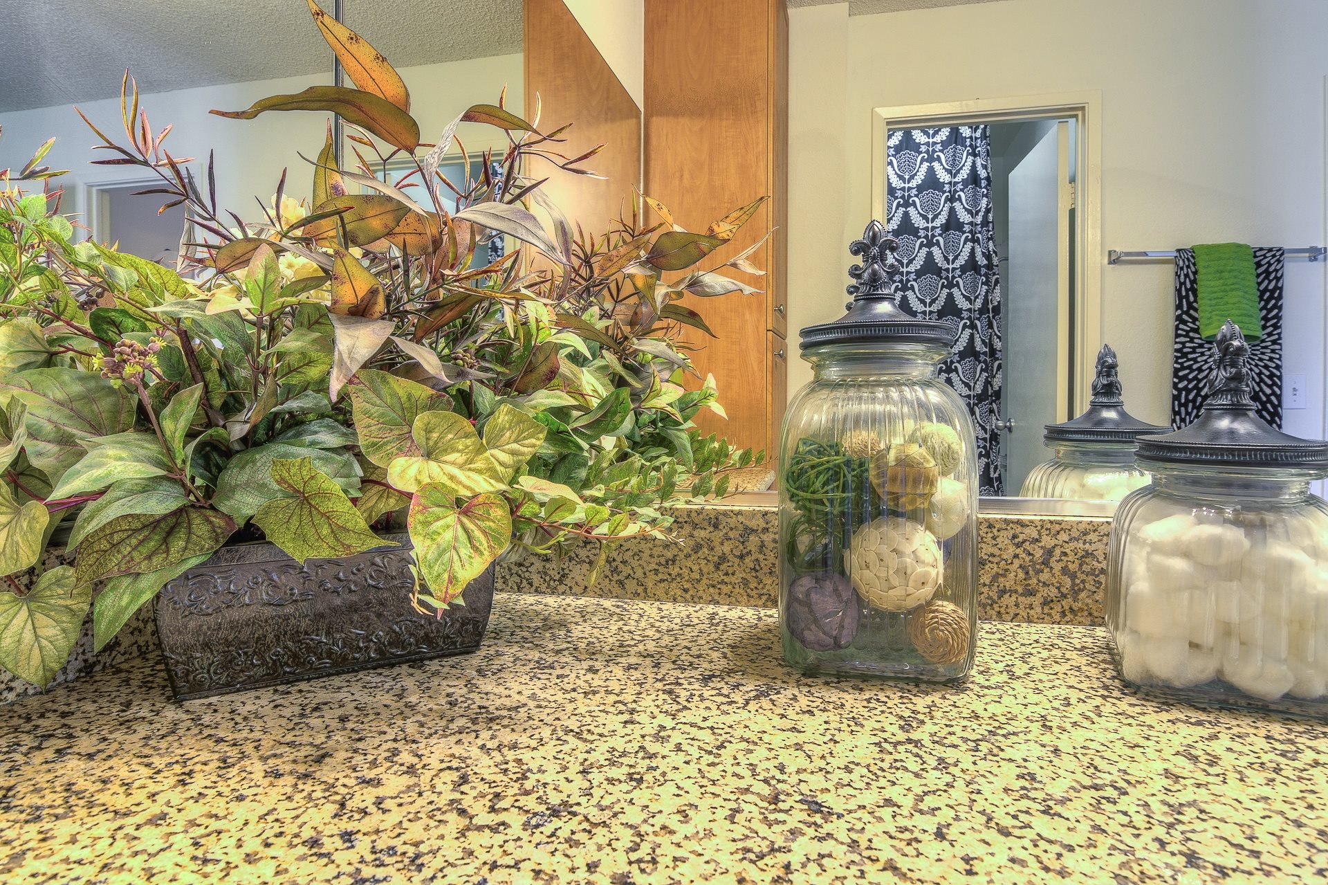 A plant in a pot sits on a countertop next to a jar with a plant inside.,A plant in a pot sits on a countertop next to a jar with a plant inside.